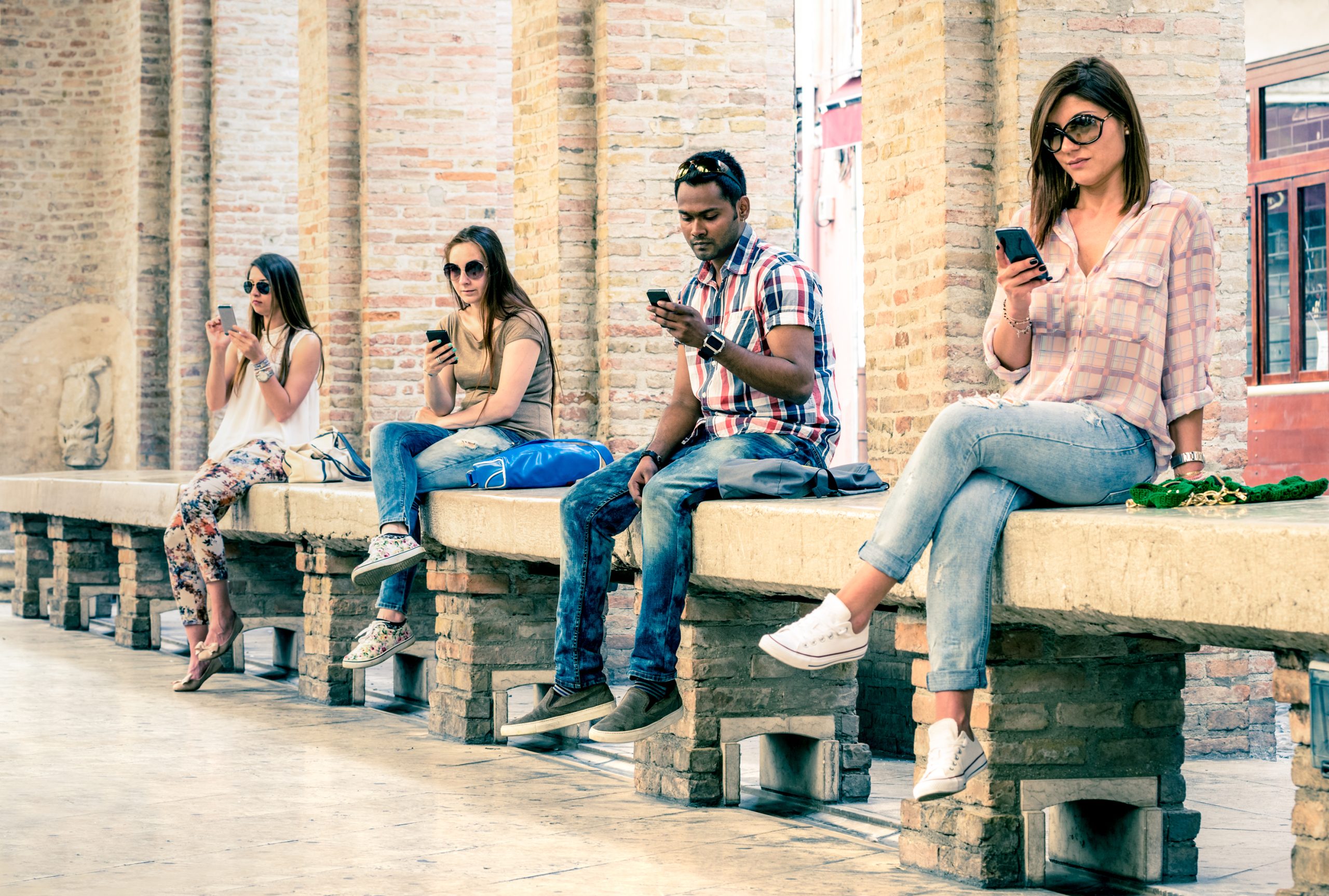 Group of young multiracial friends using smartphone with mutual Group of young multiracial friends using smartphone with mutual disinterest towards each other - Technology addiction in actual lifestyle - Soft vintage filtered look with main focus on male person